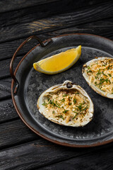 Oysters baked with cheese and herbs served with lemon on a rustic metallic plate