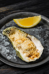 Oyster baked with cheese served with lemon on a rustic metallic plate