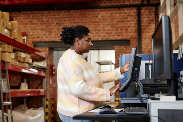 Side view portrait of adult black woman using computer while setting up printing machines in...