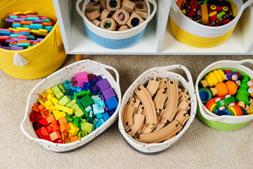 Colorful storage baskets on shelves. White shelving with rainbow wooden toys in cloth stylish baskets. Organizing and storage ideas in nursery. Interior design.