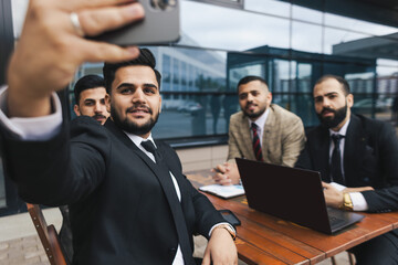 Naklejka na ściany i meble Business people outdoor meeting. Friends business partners take a selfie at a meeting. An international group of men in suits sit at an outdoor table and talking.
