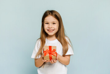 Fototapeta premium A female child holds a box with a Christmas present in her hand. Isolated on blue background