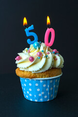 Tasty cupcake with with candles 50 fifty on a black background. Cake with white cream. Photo in low key. Festive dessert and congratulations.