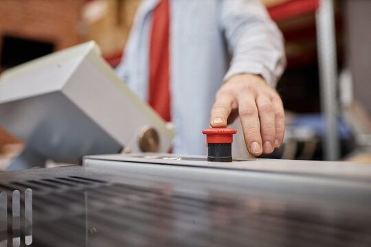 Close up of young man pressing red button on printing press in industrial shop, copy space