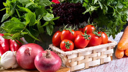 Fresh seasonal greens and cherry tomatoes in a wicker basket in front of a black background, mint, parsley, pepper, carrot, lettuce