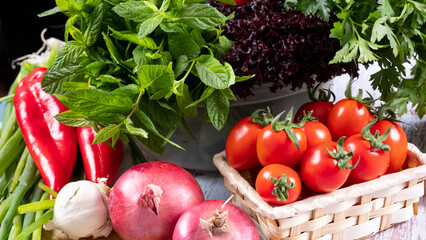 Fresh seasonal greens and cherry tomatoes in a wicker basket in front of a black background, mint, parsley, pepper, carrot, lettuce