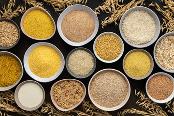 Various grain cereals in bowls, top view on a brown background with bowls of cereals and ears of oats
