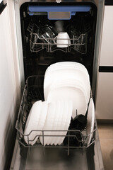 Open dishwasher with white and black clean dishes after washing in the kitchen. Clean the dishes in an open dishwasher.