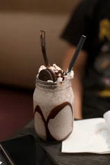 Fotobehang Vertical shot of a cookie milkshake in a glass jar with a straw on the blurred background © Aditya Anil/Wirestock Creators