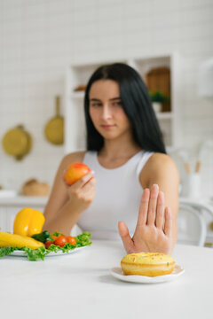 Woman who refuses sweet food, preferring healthy nutrition, gadflies and fruits, sitting at the table in the kitchen