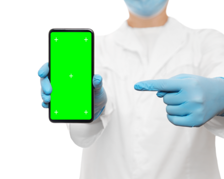 Cropped shot of a doctor in a blue medical mask and gloves holding smartphone with greenscreen and tracking points, pointing finger on it. Isolated on white, copy space.
