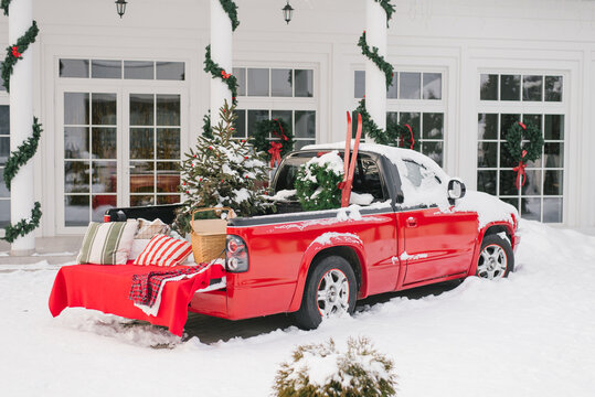 Red Pickup Truck With Christmas New Year Decor In The Courtyard Of A Suburban Snow House