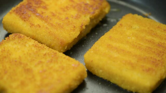 Fish sticks. The process of cooking fish sticks in a pan, close-up. Breaded fish fillet.