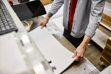 High angle view of man putting stack of paper in printing machine at publishing shop, copy space