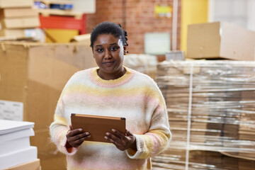 Waist up portrait of smiling black woman holding digital tablet at printing shop and looking at camera