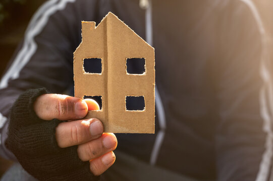 Obdachloser h&auml;lt ein Haus aus Pappe in der Hand