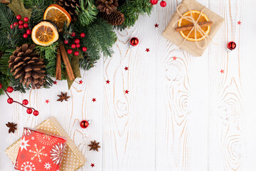 Christmas holiday background with wooden deer, christmas tree decorated with pine cone, beads and gifts wrapped in craft paper, dried oranges on white rustic wooden background, flat lay, copy space.