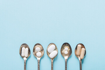 Healthy supplements on teaspoons on a pastel background. Tablets and pills.