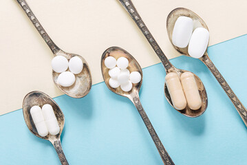 Healthy supplements on teaspoons on a pastel background. Tablets and pills.