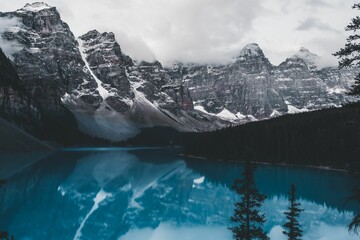 Long shot of lake moraine reflecting surrounding trees and snow-capped mountains.