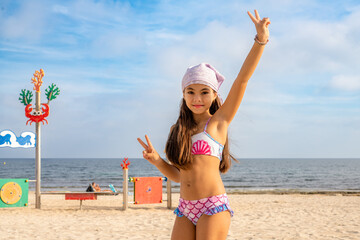 Little cute child girl in playground on the beach with smile on summer vacation. Happy children kid...