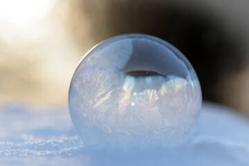 A frozen bubble in the snow with bokeh in the background. Beautiful frosty patterns on a frozen soap bubble. winter, frosty background. Frozen bubble at sunset light. soap bubble on snow close up