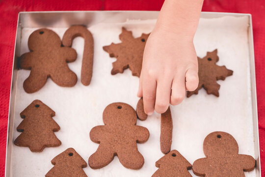 Overhead view of a child's hand reaching for a freshly baked homemade s snowflake gingerbread cookie