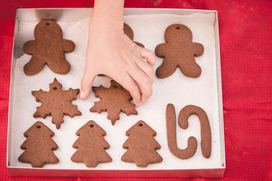 Overhead view of a child's hand reaching for a freshly baked homemade s snowflake gingerbread cookie