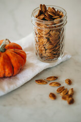 Roasted pumpkin seeds spill out of a glass jar with a small orange pumpkin in view