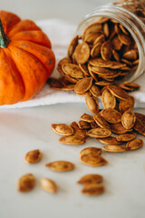 Roasted pumpkin seeds spill out of a glass jar with a small orange pumpkin in view