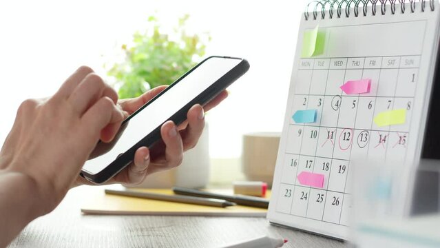 A business woman's hands are taking notes on a calendar and using a mobile phone to plan meetings and events.