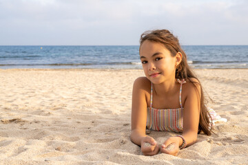 Fototapeta na wymiar Little beautiful smiling girl lying on the sand at the beach.