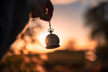 Silhouette einer Taschenuhr wird an einer Kette vor einen goldenen Sonnenuntergang gehalten.