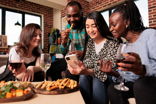 Smiling Young Adults, Bunch People Staring, Looking Movies At Cell Phone, Laughing, Eating Bread Sticks, Drinking Glasses Of Wine, Talking, Living Together At Home Made Party.