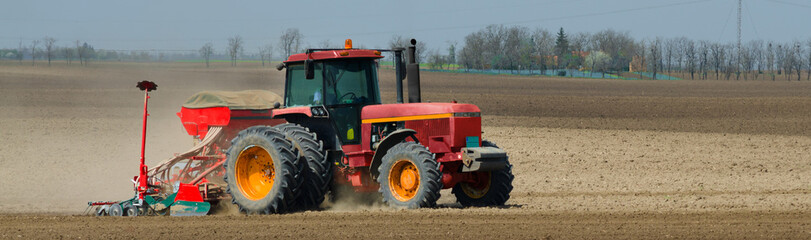 Red tractor sowing on the agricultural field on a sunny spring day