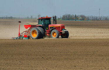Red tractor sowing on the agricultural field in spring