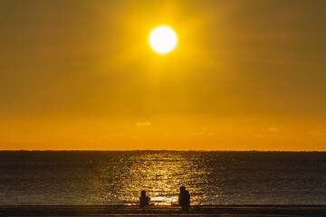 Fototapeta premium Silhouette of two people sitting on the beach just after sunrise