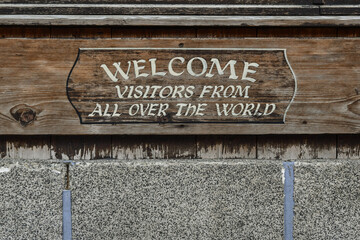 Close-up of a sign that says: "Welcome visitors from all over the world" on a stone and wood wall of the mountain town, Chamonix, Haute Savoie, France