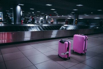 Selective focus on two pink luggage travel wheeled suitcases next to the baggage conveyor belts in...