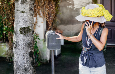 a middle-aged woman wearing a hat check the mailbox at her home. traditional mail concept.