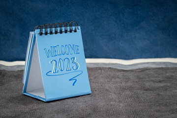 Welcome 2023 - handwriting in a desktop calendar against abstract paper landscape, New Year concept
