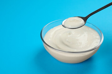 Fototapeta na wymiar Eating tasty organic yogurt from bowl on light blue background, space for text