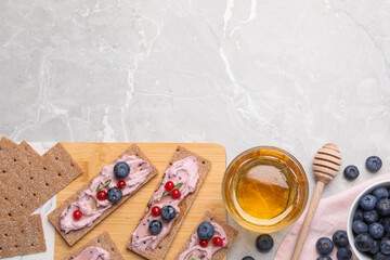 Obraz na płótnie Canvas Tasty cracker sandwiches with cream cheese, blueberries, red currants, thyme and honey on light grey marble table, flat lay. Space for text
