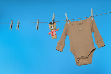 Baby onesie and bear toy drying on laundry line against light blue background, space for text