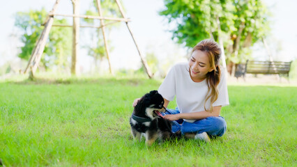 Naklejka na ściany i meble Happy young asian woman playing and sitting on grass in the park with her dog. Pet lover concept