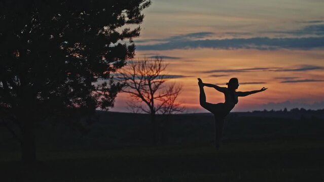 Anonymous woman doing Parivritta Natarajasana pose at sunset