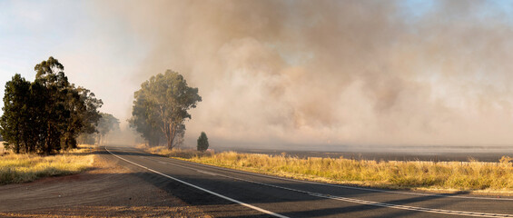 Panoramic image showing bush fire smoke blowing over a country highway in rural farming Victoria,...