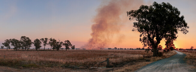 Panoramic image of a plume of balck smoke rising at sunset from a line of wild fire in the distant...