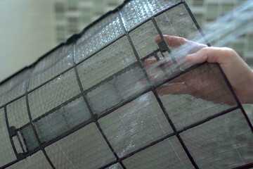 Asian woman cleaning a dirty and dusty air conditioning filter in her house. Housewife removing a...