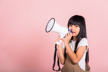 Asian little kid 10 years old shouting by megaphone at studio shot isolated on pink background,...